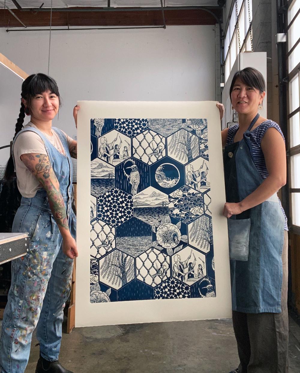 Artists Saiyare Refaei and Yoshi Nakagawa standing on either side holding their print "Sound", which is blue and white