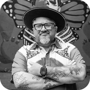 A black and white image of a man crossing his arms in front of a large artwork painted on a wall