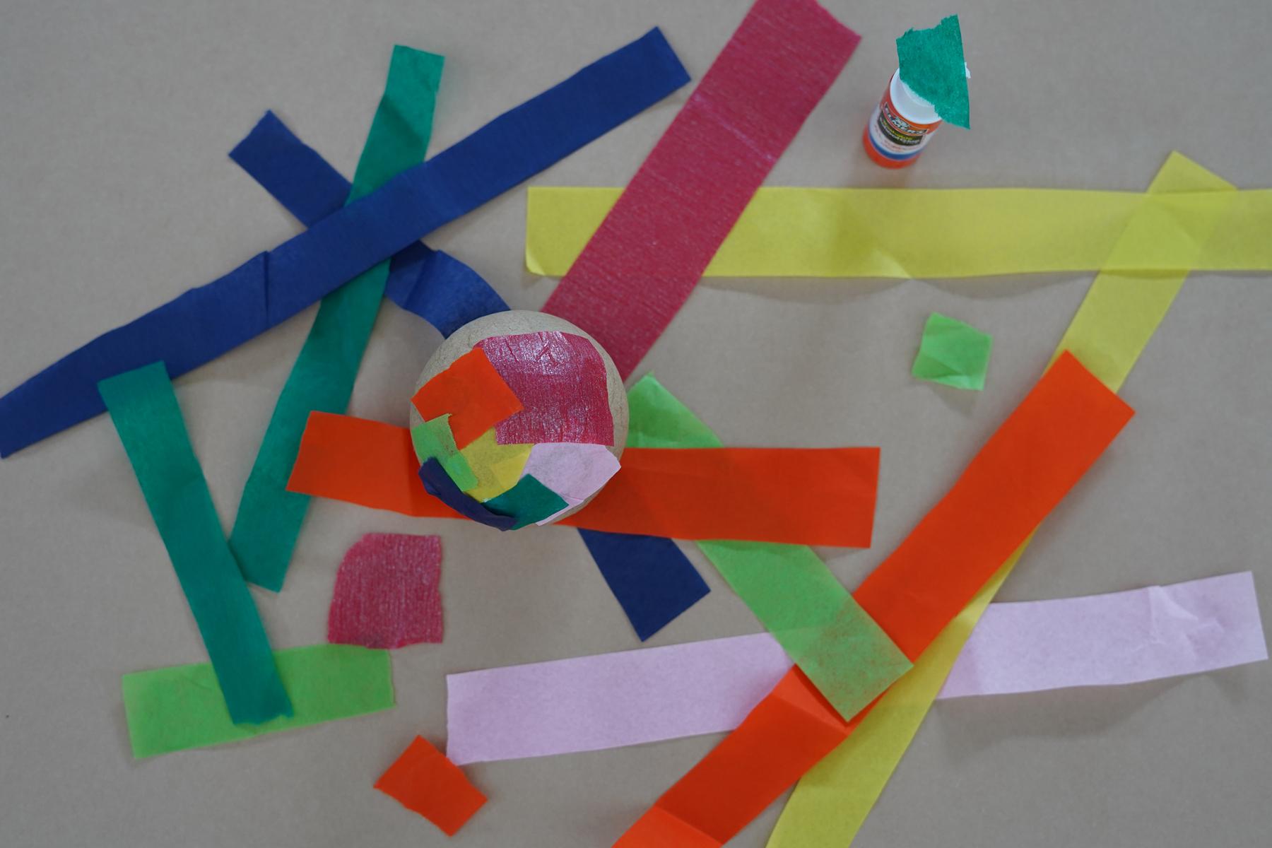 Photo of a cardboard ball with pieces of tissue paper on it and other tissue paper around it on a tabletop