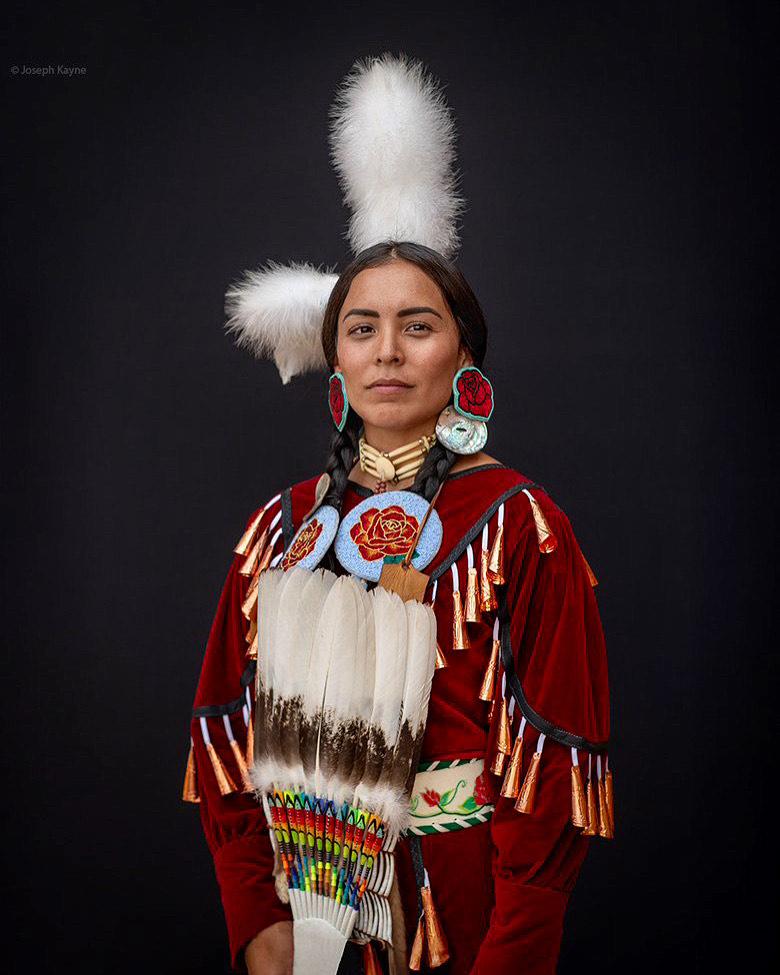 A woman in traditional western american indigenous clothing, including large head feathers