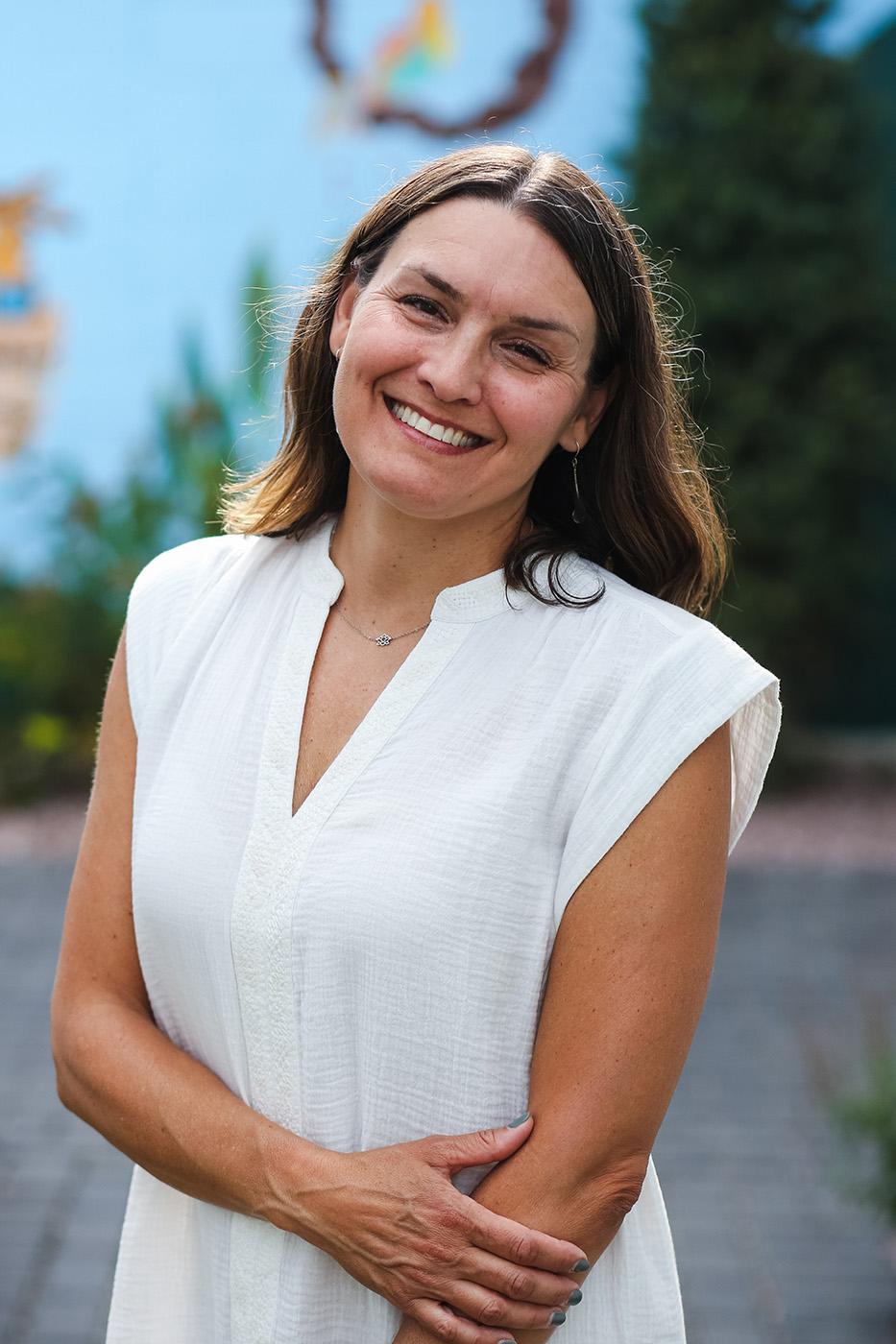 Professional headshot style photograph of a smiling woman wearing a white top