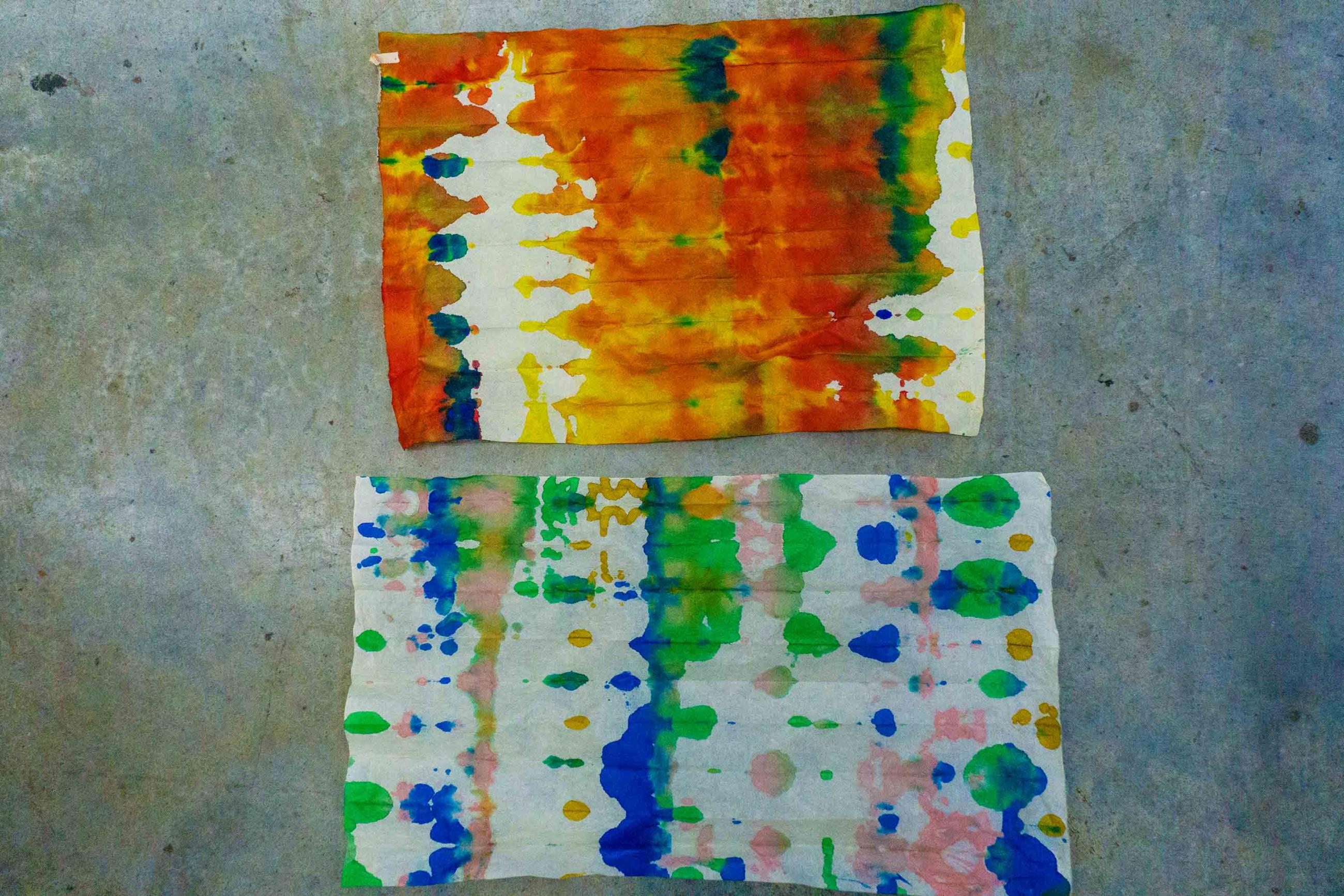 Photo of two artworks: one is primarily orange and yellow; the other green, pink, and blue