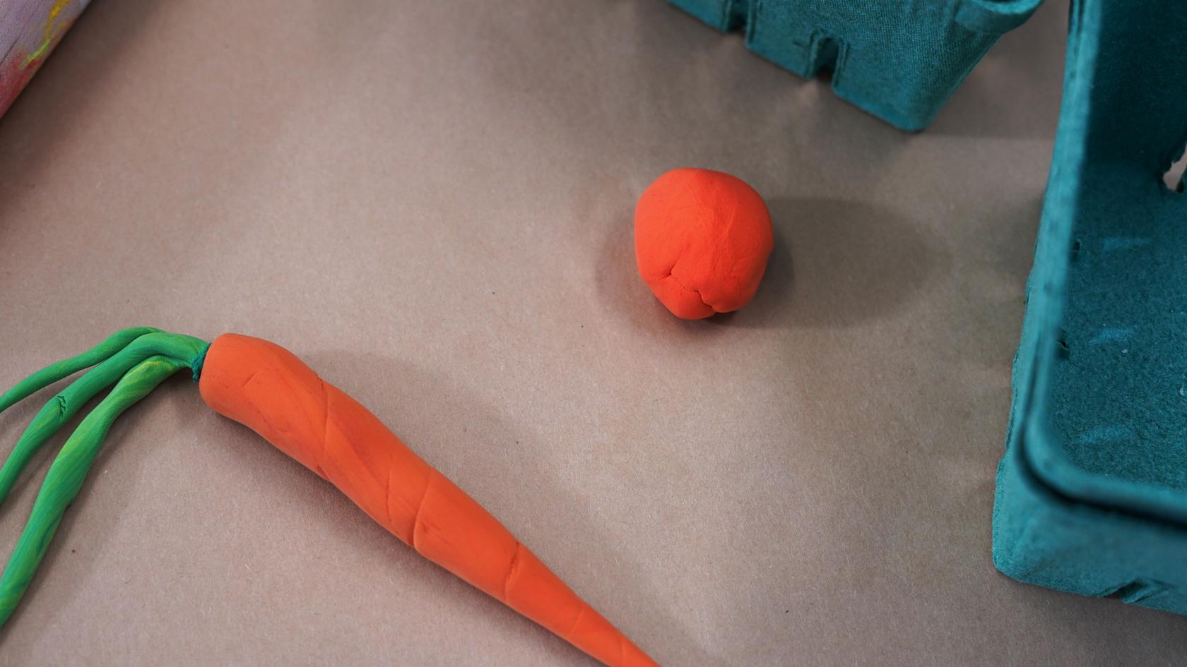 Photo of a ball of orange modeling clay and a carrot made from modeling clay