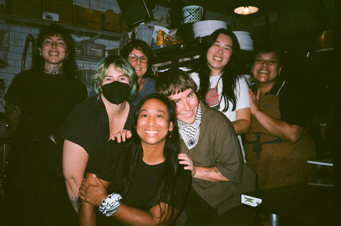 A group of people, including Cece Edson, gathered together smiling for the camera in a kitchen