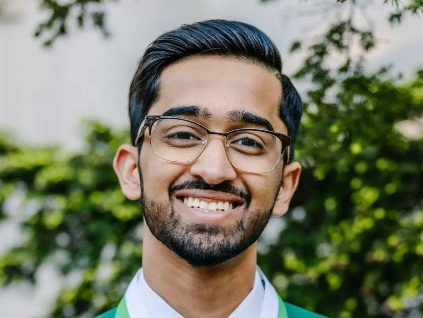 A professional headshot style photograph of a smiling younger man