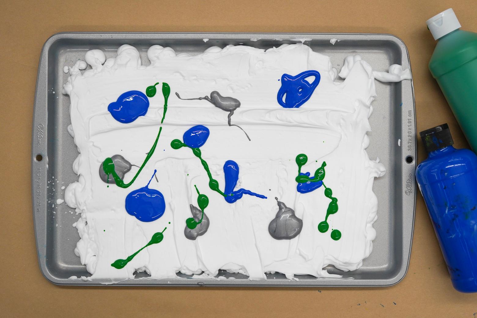 Photo of a sheet pan with shaving cream in it topped with blobs of blue, green, and gray paint