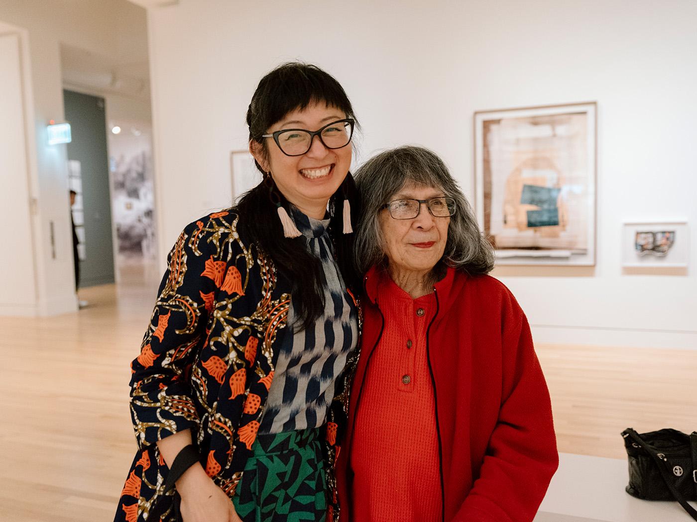 Two Asian women, one older, standing side by side and smiling in a large gallery space