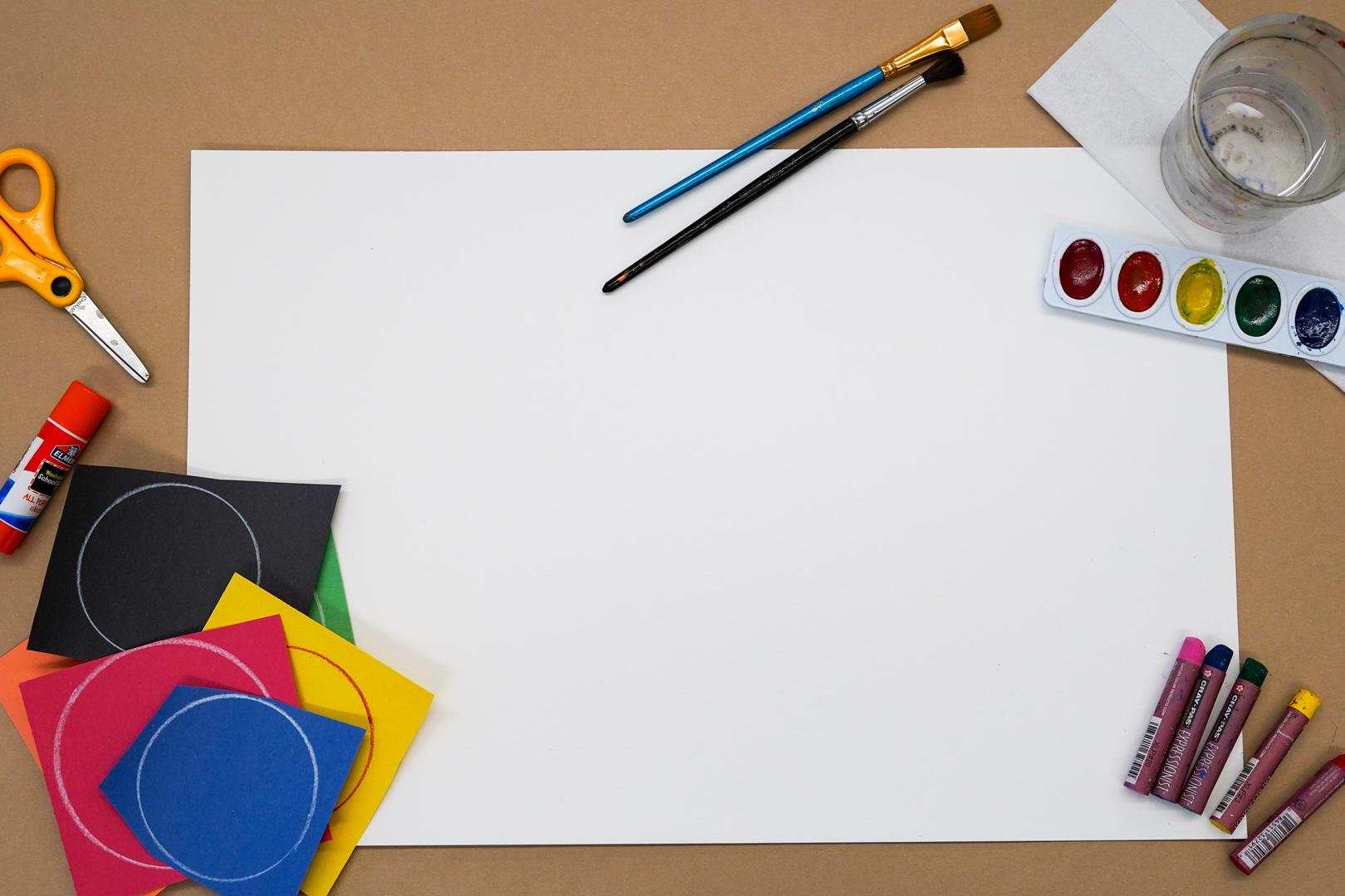 Photo of a blank white piece of paper with various art supplies around it