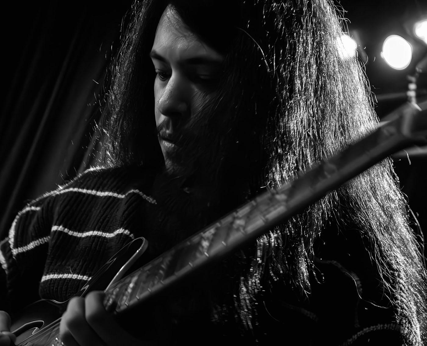 A close up black and white photo of a person with long hair playing guitar