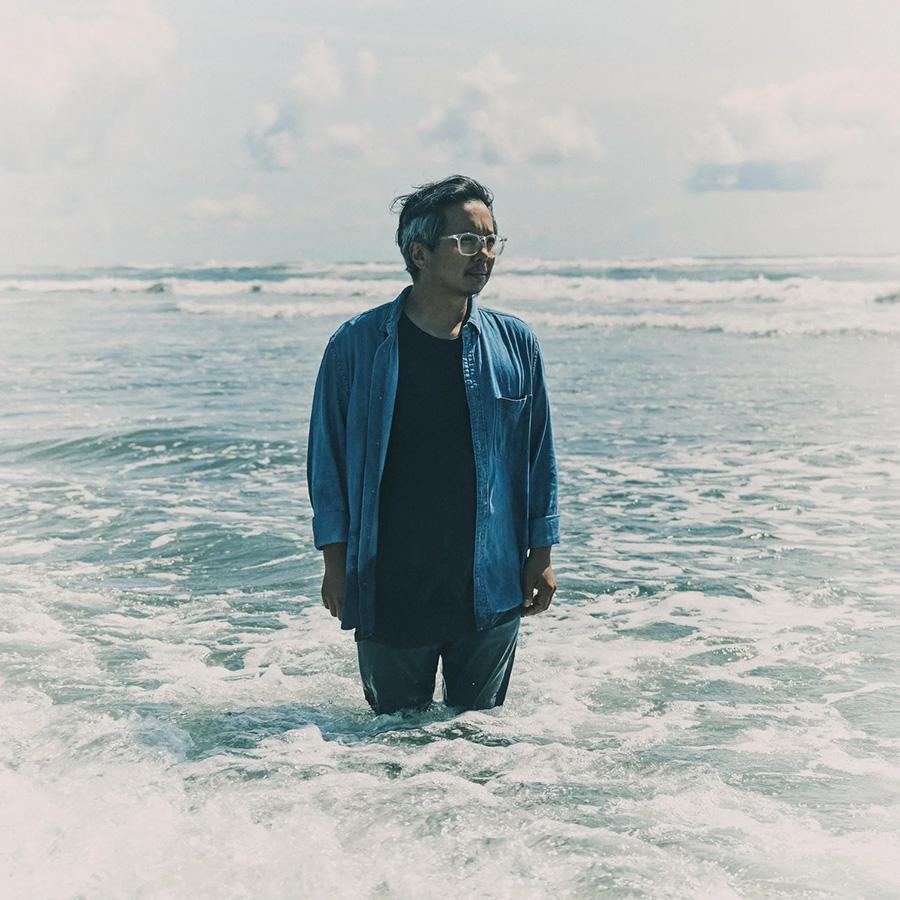 A clothed man standing up to his knees in a sea or other large body of water