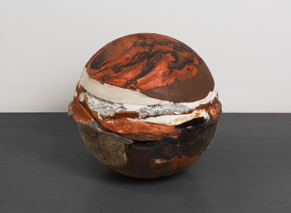 Spherical sculpture the size of a basketball, comprised of layers of melted plastic in oranges, whites, blacks and grays