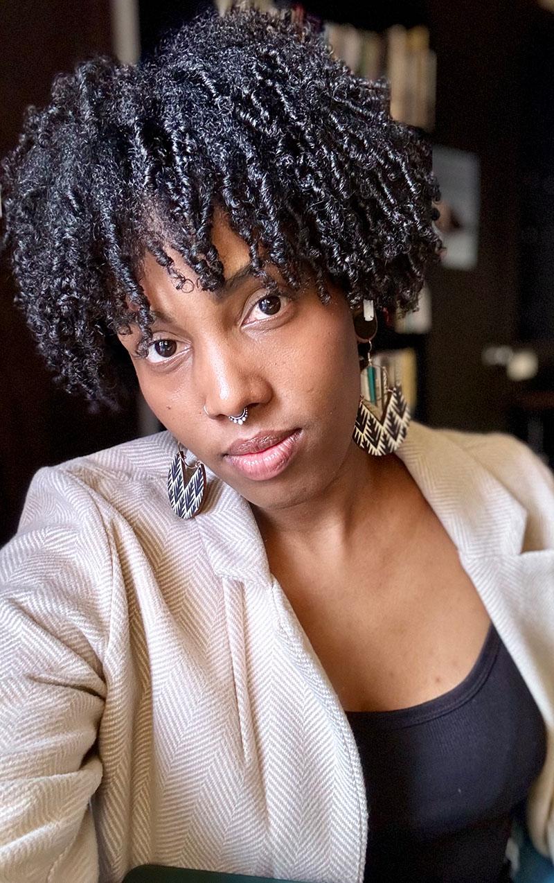 A selfied style photo of a woman wearing a light blazer and large earrings