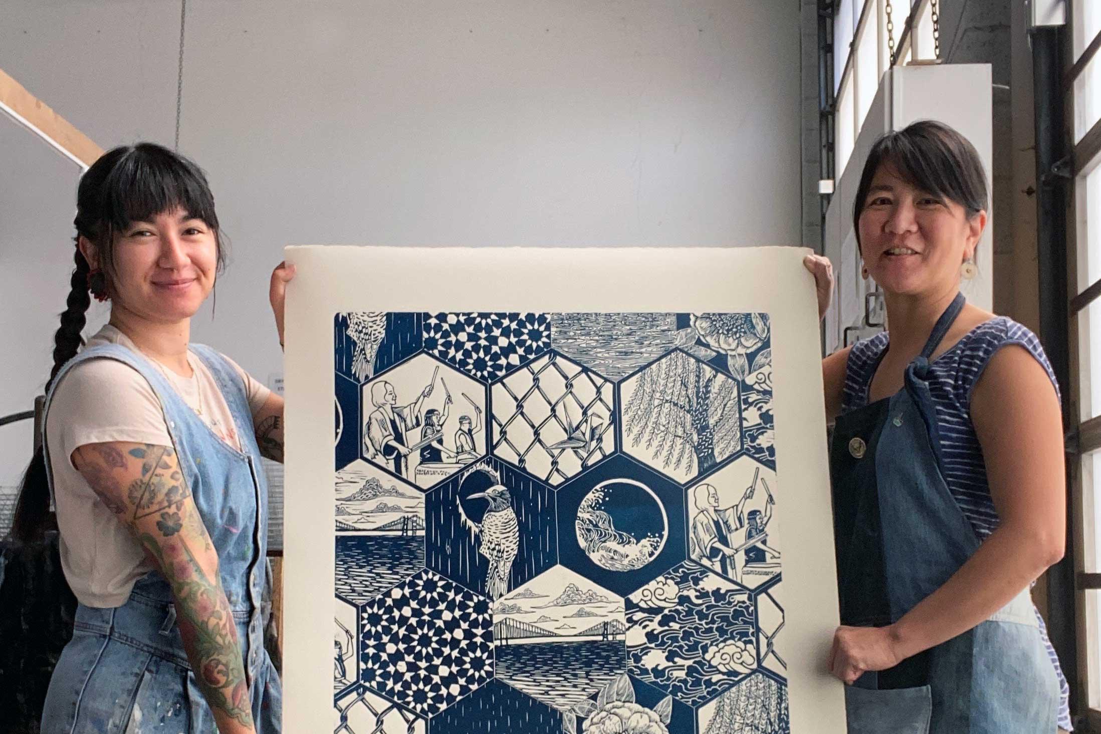 Artists Saiyare Refaei and Yoshi Nakagawa standing on either side holding their print "Sound", which is blue and white