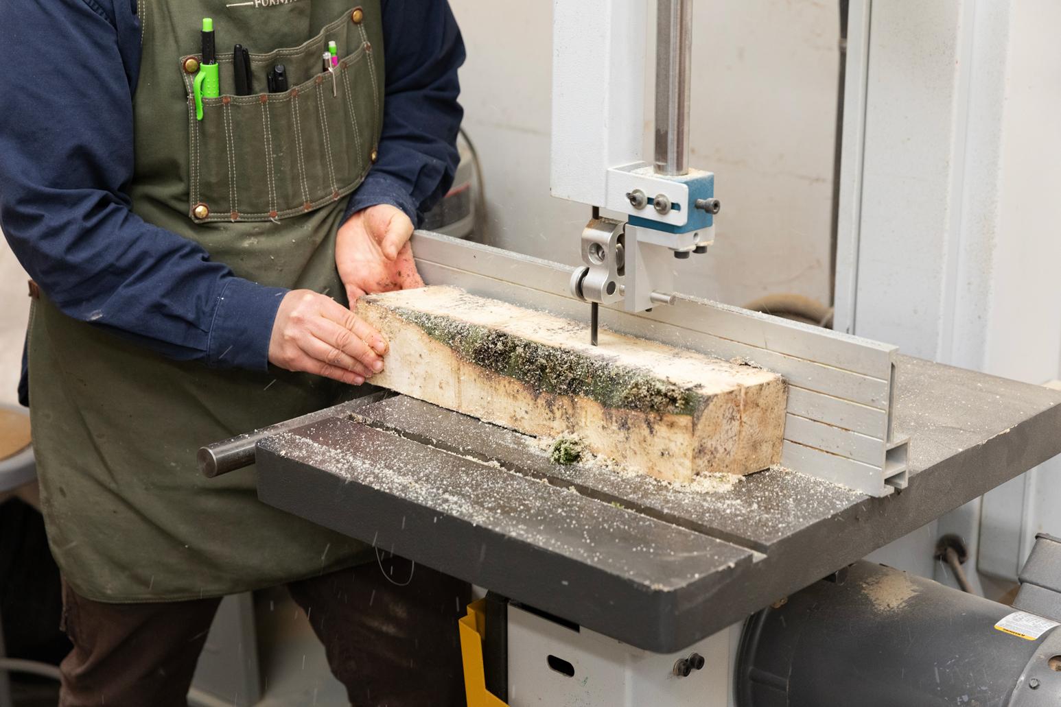 Hands guiding a piece of wood through a band saw
