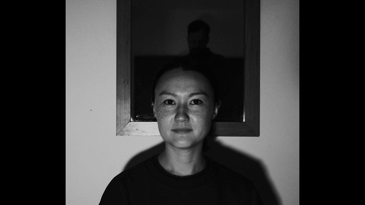 A black and white image of a woman's face in front of a dark window