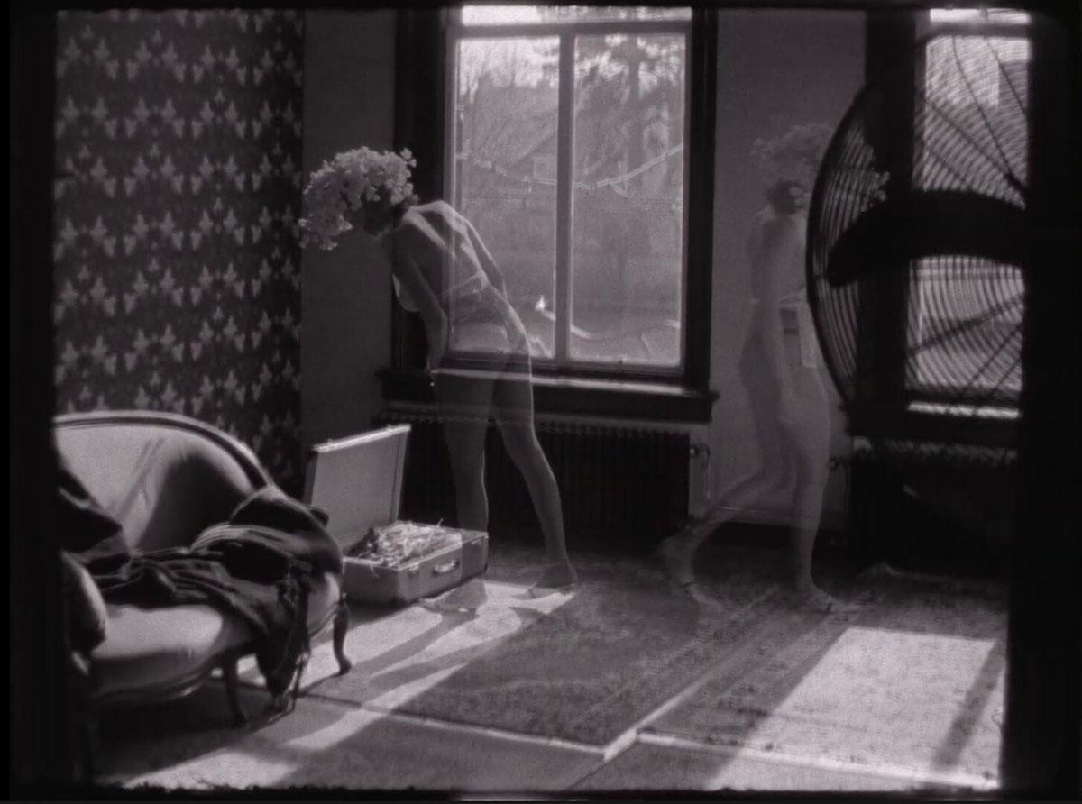 A sepia toned still from an image with ghostly female figures moving about a room