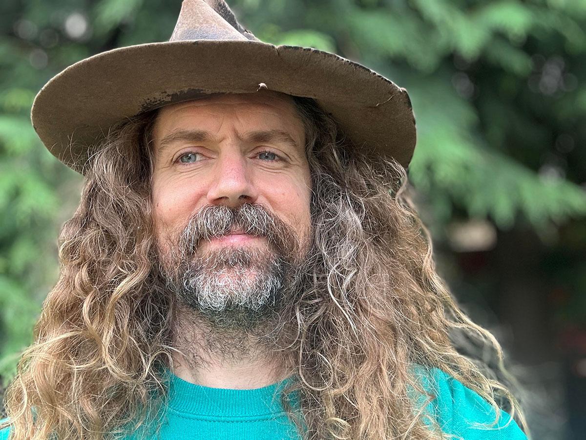 A man with long hair and a short beard in a wide brimmed hat