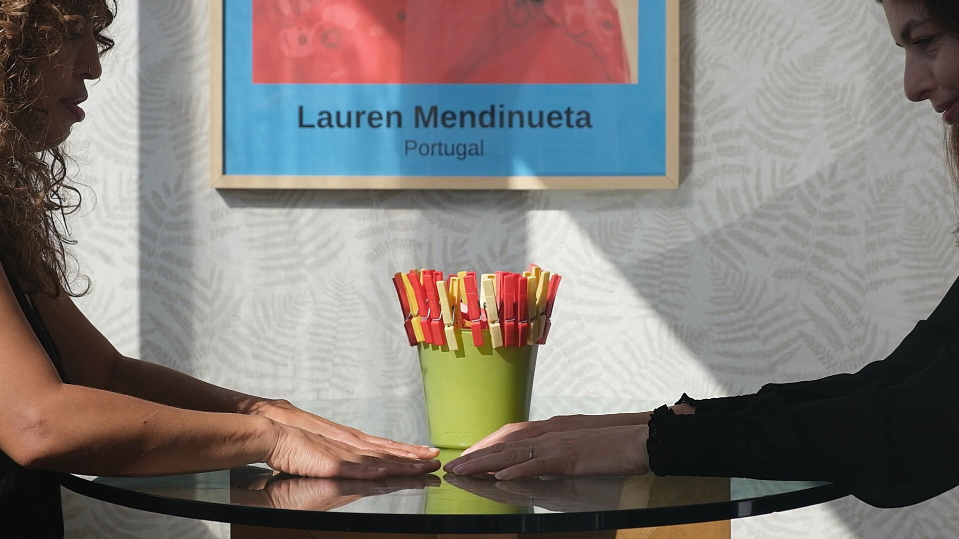 Two people sitting and facing each other across a small circular table. Both people have their palms on the table.