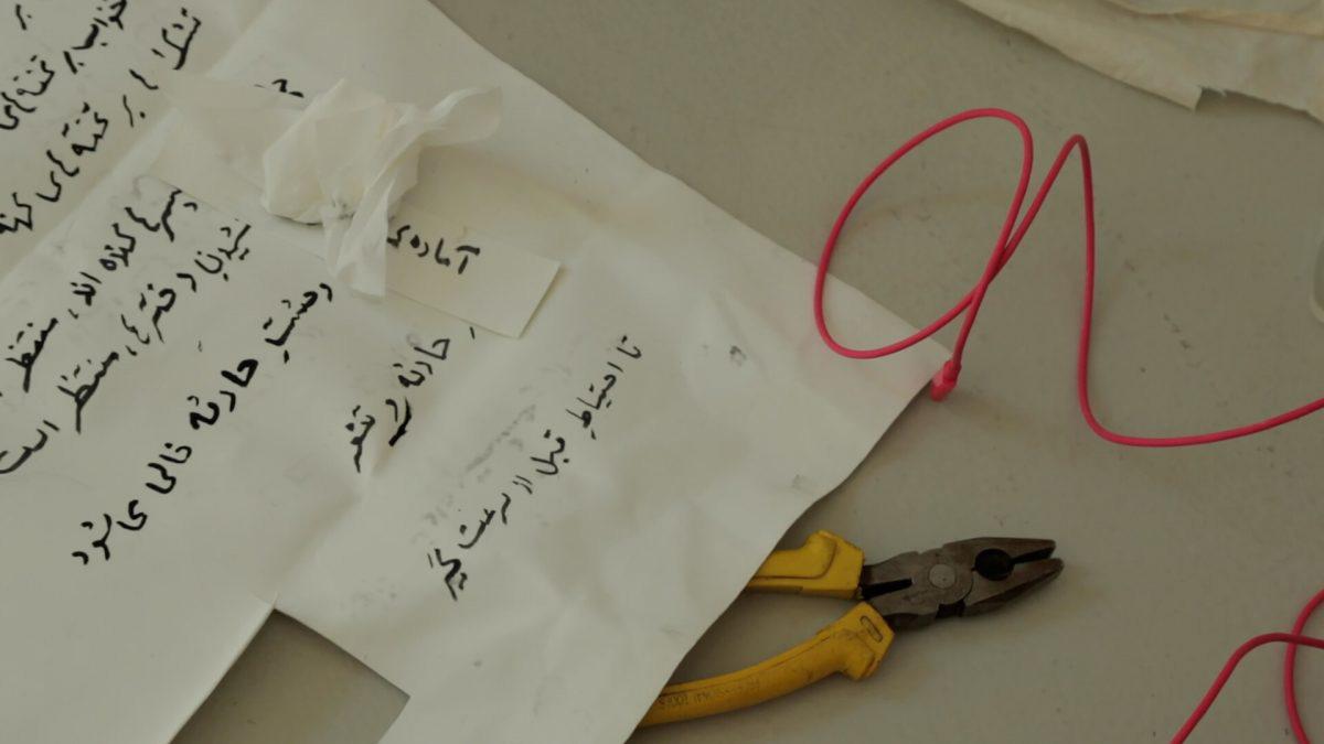 Still from a film of a piece of paper with Arabic writing and a pair of pliers