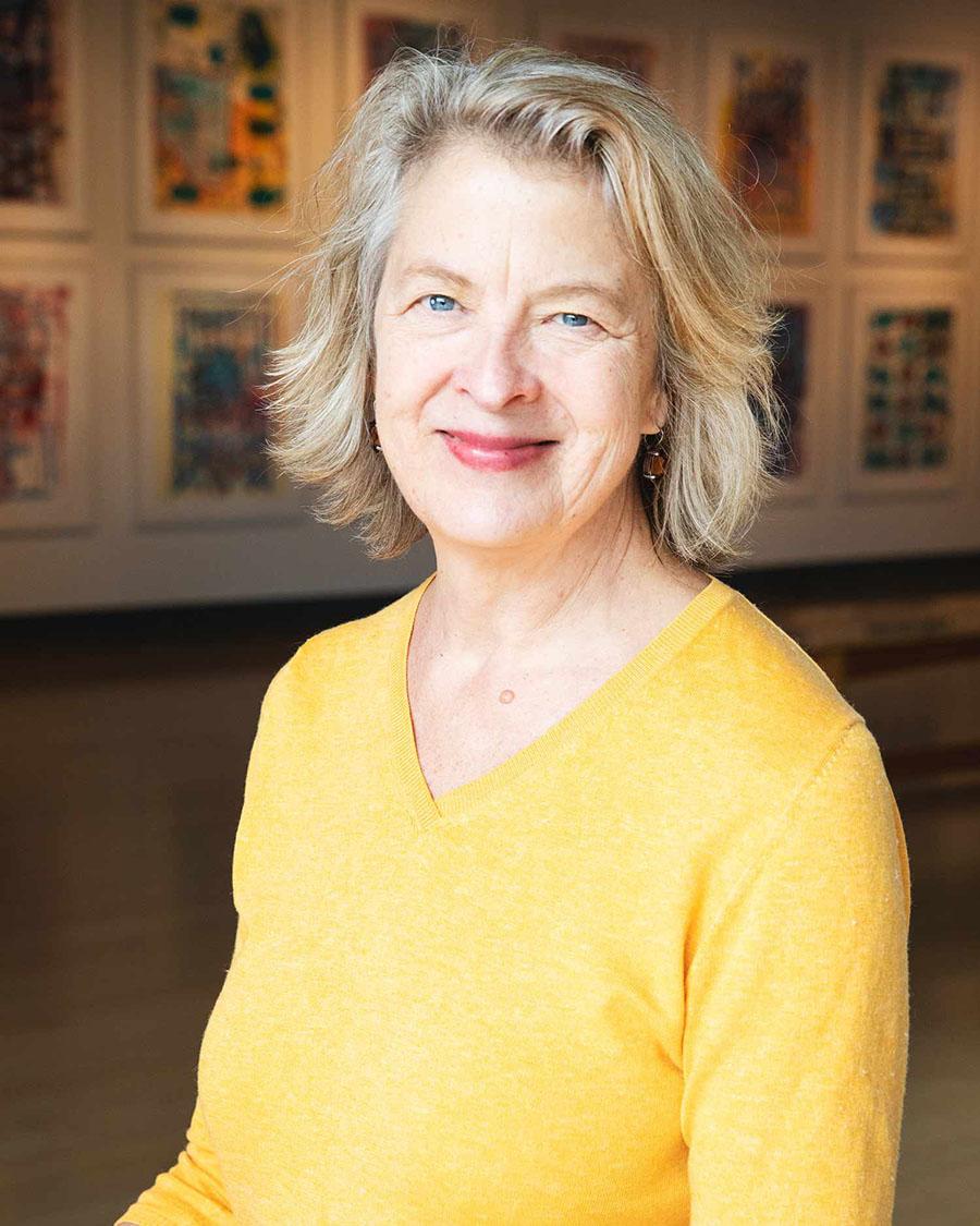 A formal headshot style photograph of a woman wearing a yellow top