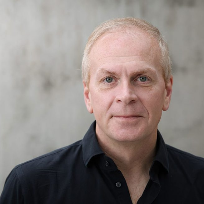 A photo of a man with short white hair and a black button-up shirt