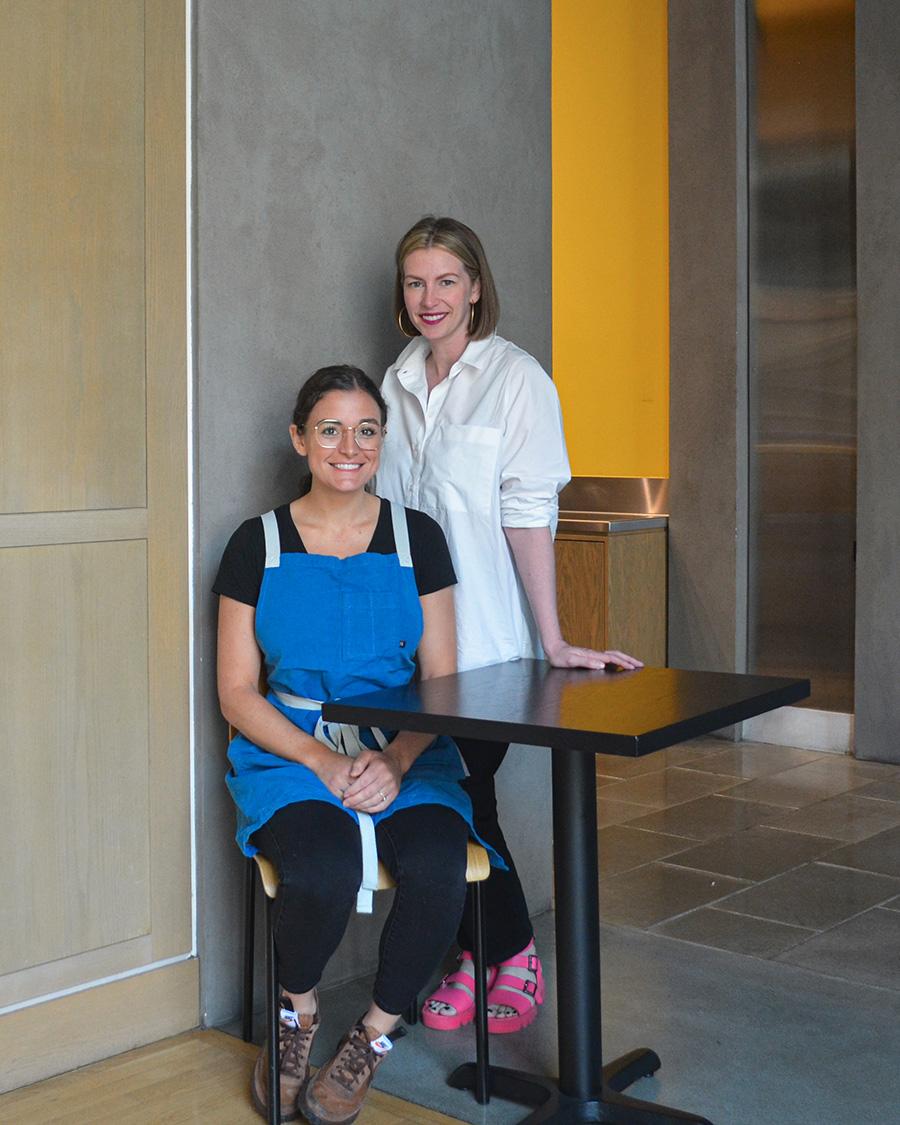 Two women next to a table, one standing and one sitting