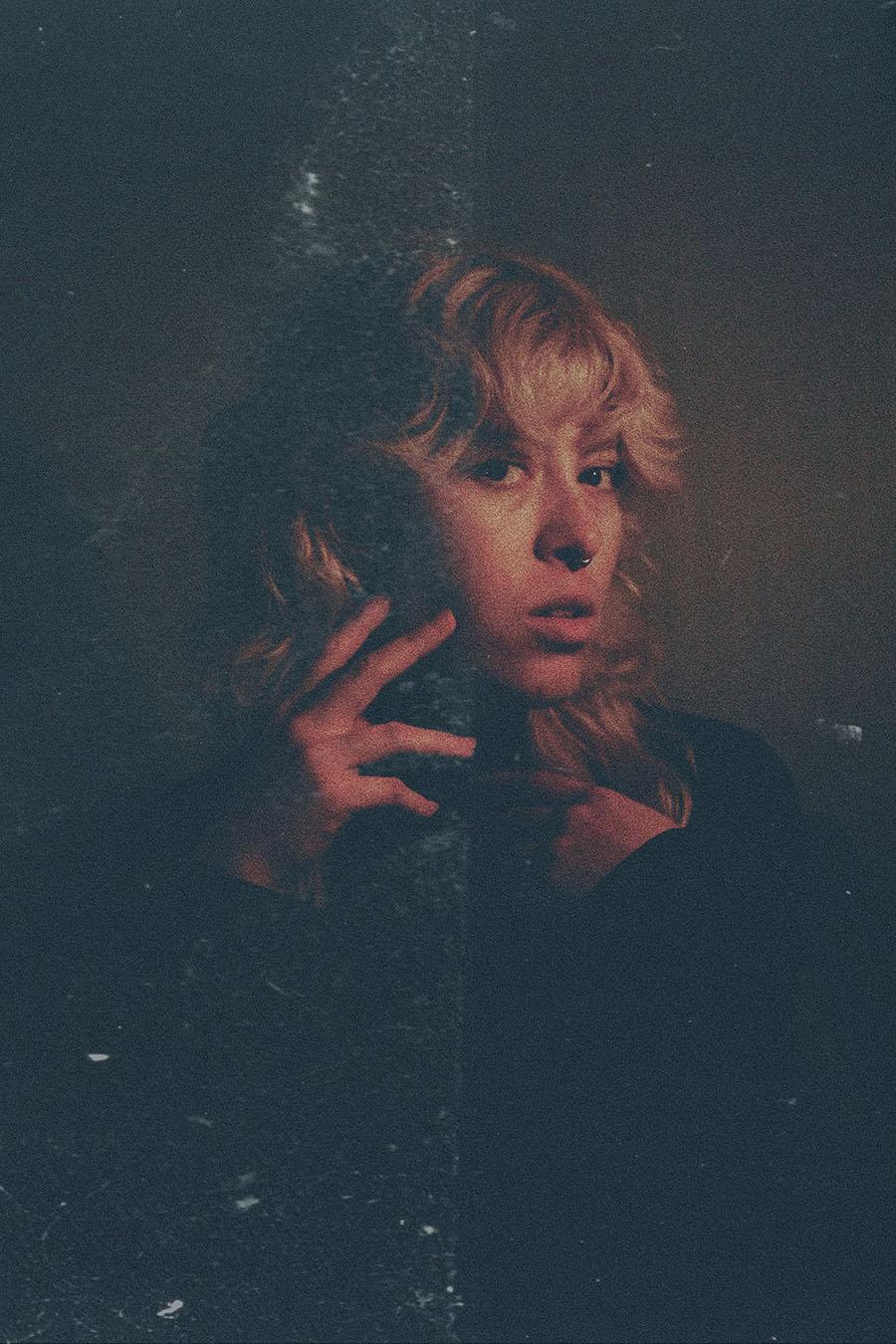 A dark photograph of a younger woman with wavy blonde hair processed to look like expired film