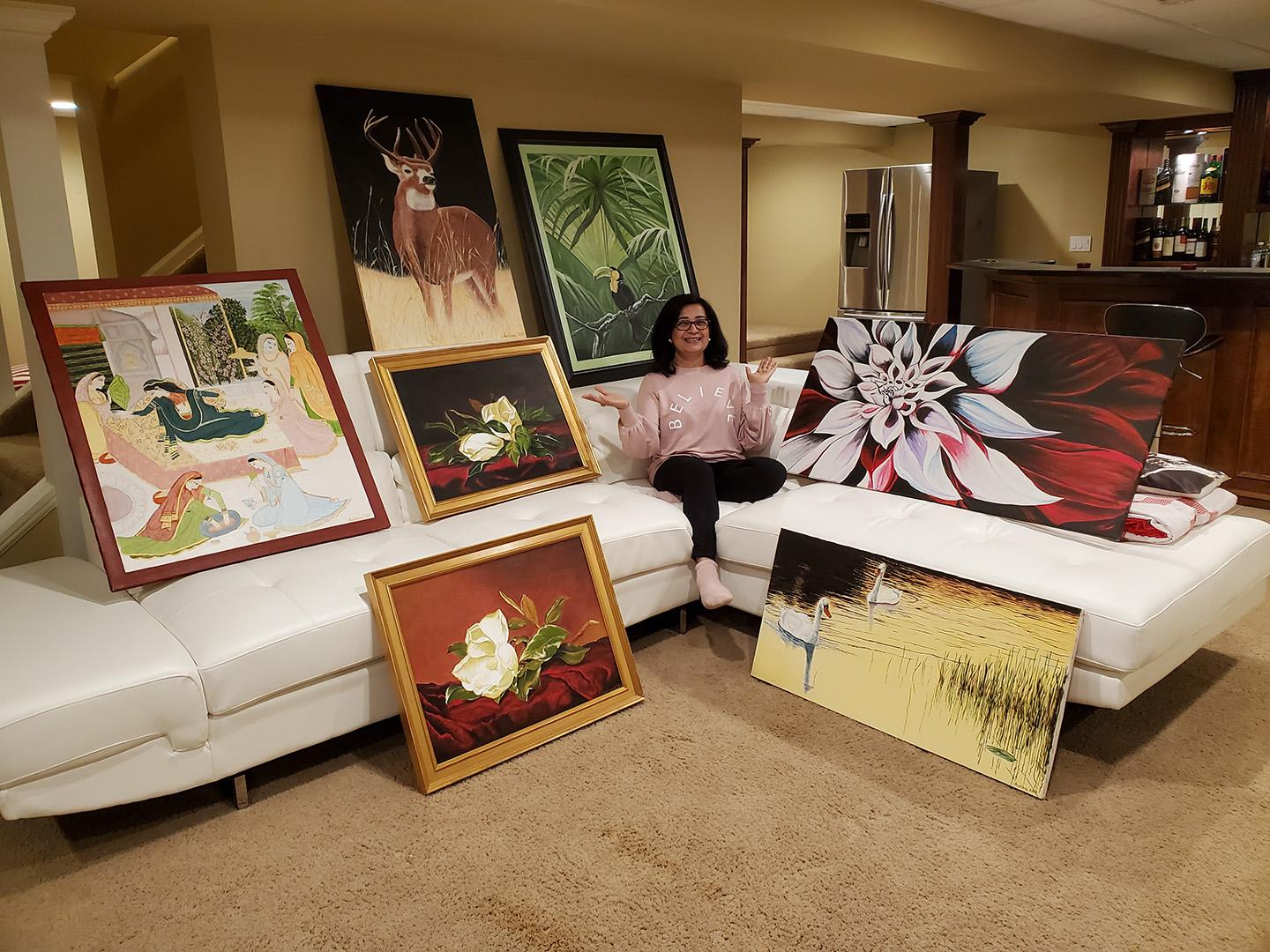 A woman sitting on a sectional couch surrounded by large painted works of art