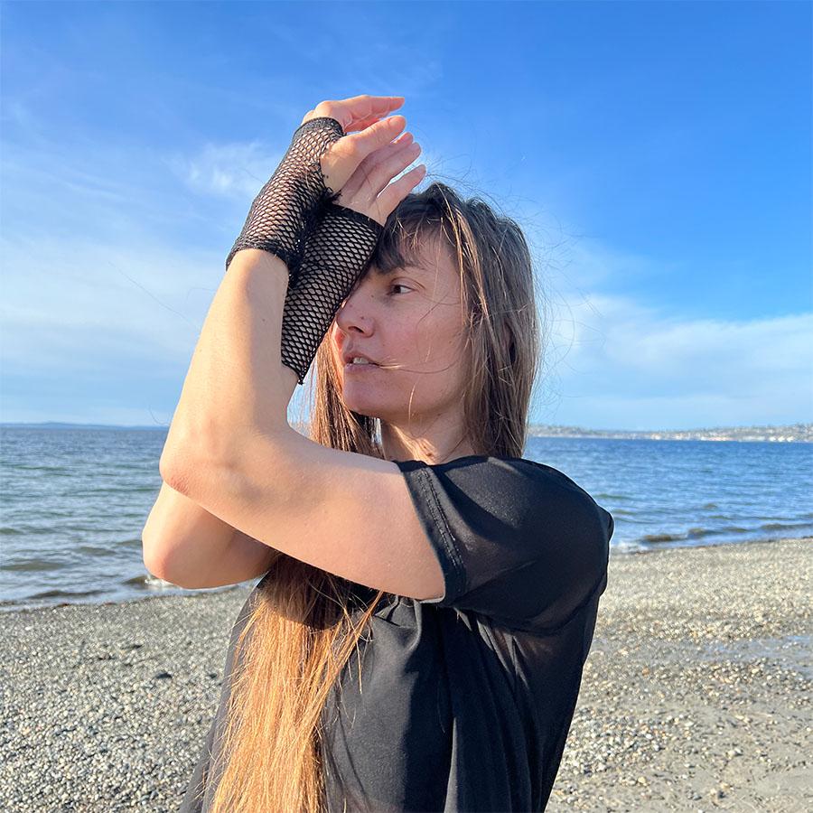 A person standing on a beach crossing their arms in front of their face